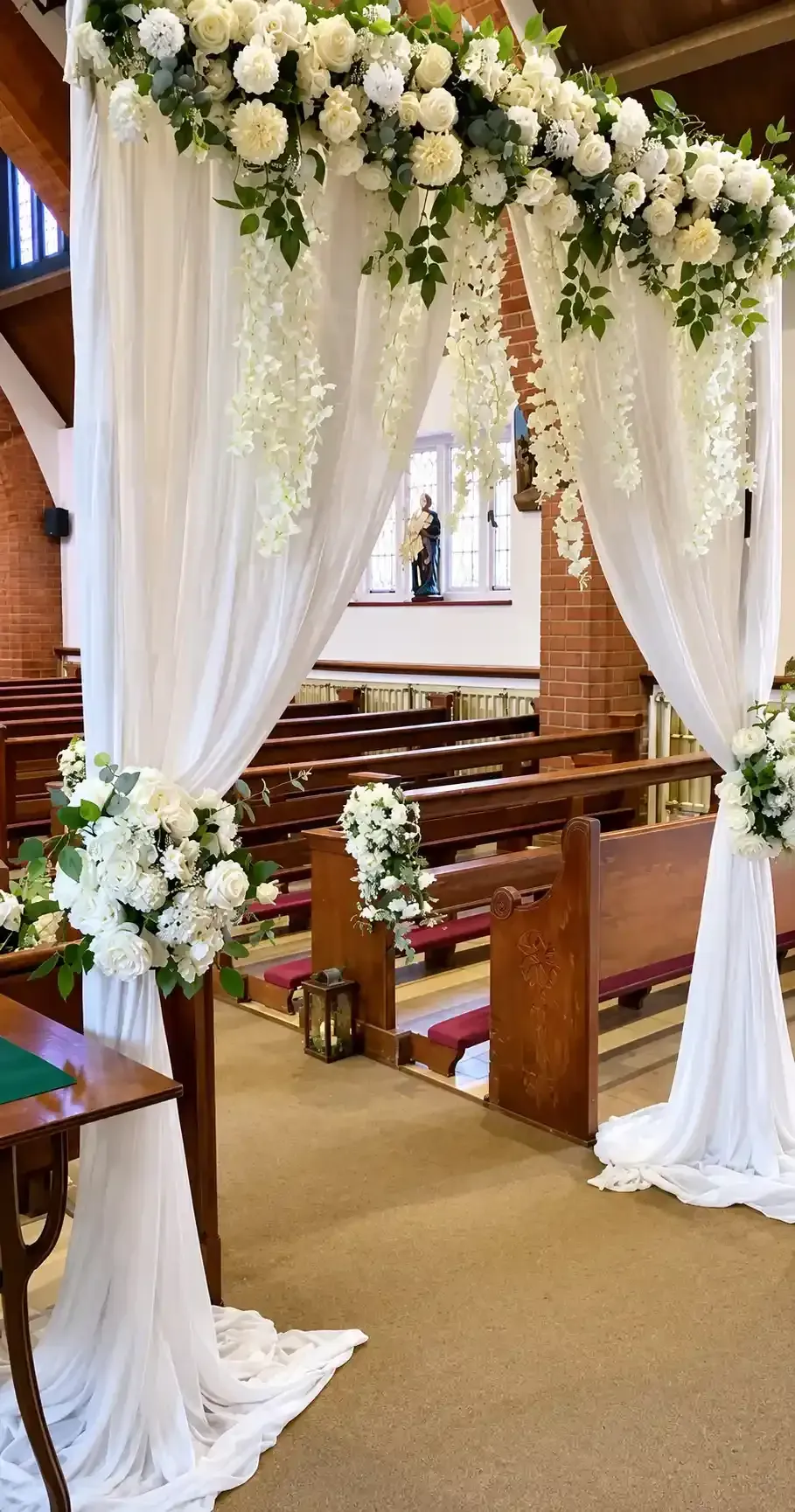 Arco nupcial floral blanco con tela drapeada en el pasillo de una iglesia.