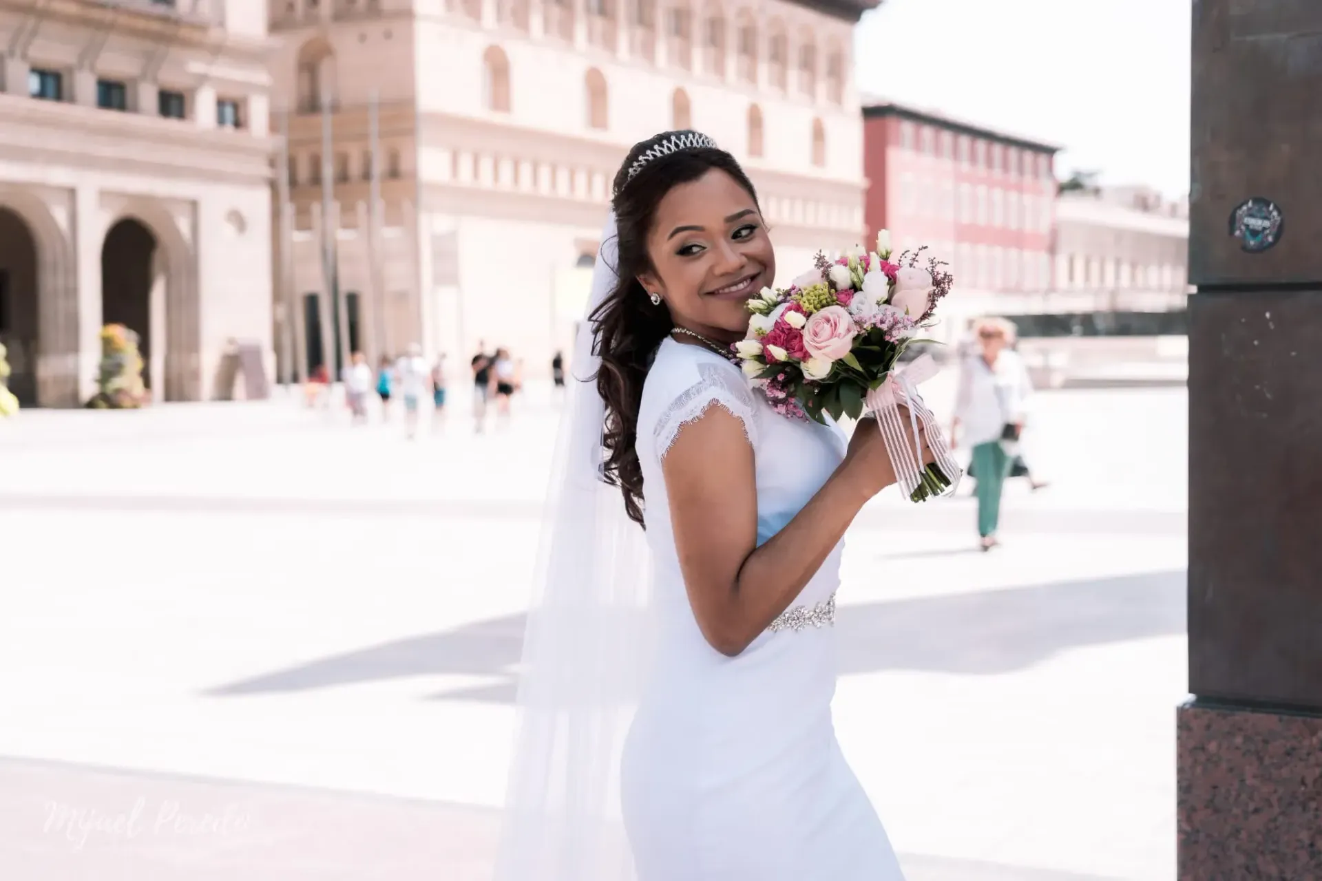 Novia con vestido blanco sonriendo y sosteniendo un ramo en un patio luminoso