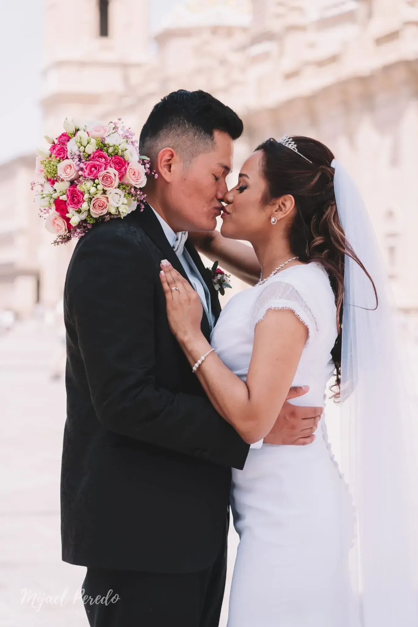 Pareja de recién casados besándose al aire libre, la novia con vestido blanco