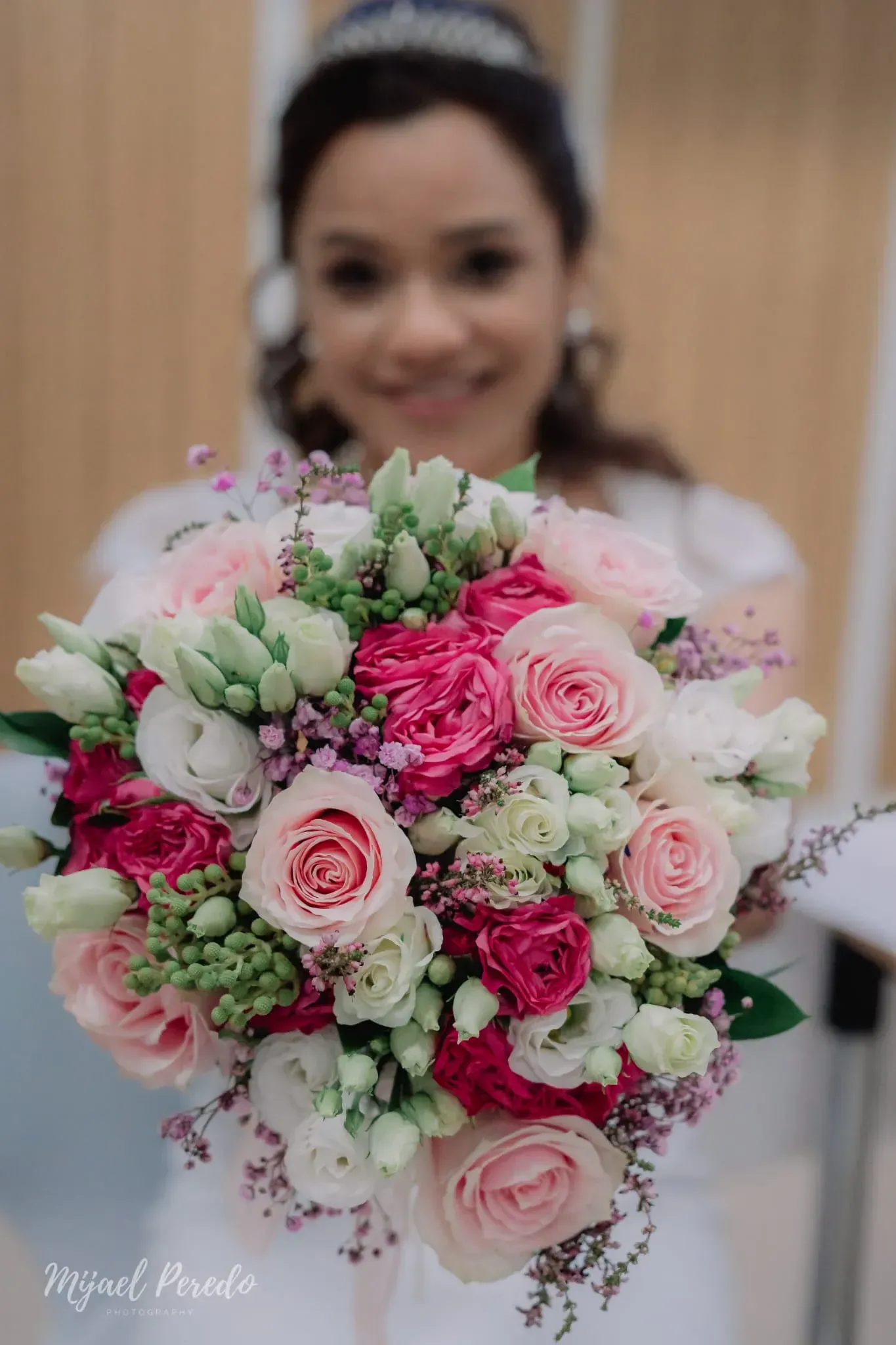 Mujer con un ramo de rosas rosas y blancas, sonriendo en el interior de un edificio.