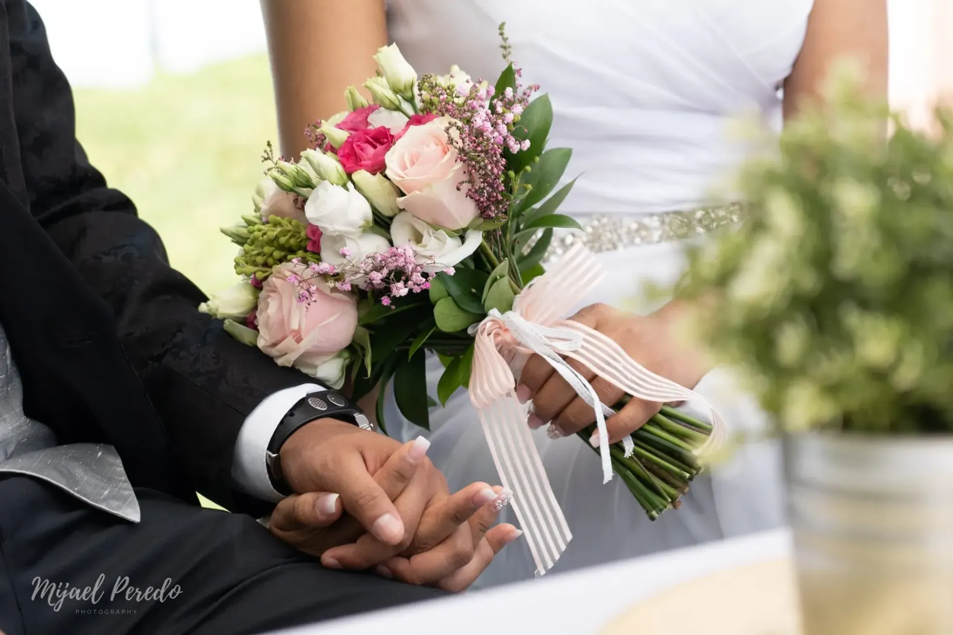 Los novios tomados de la mano junto a un ramo de novia rosa y blanco.