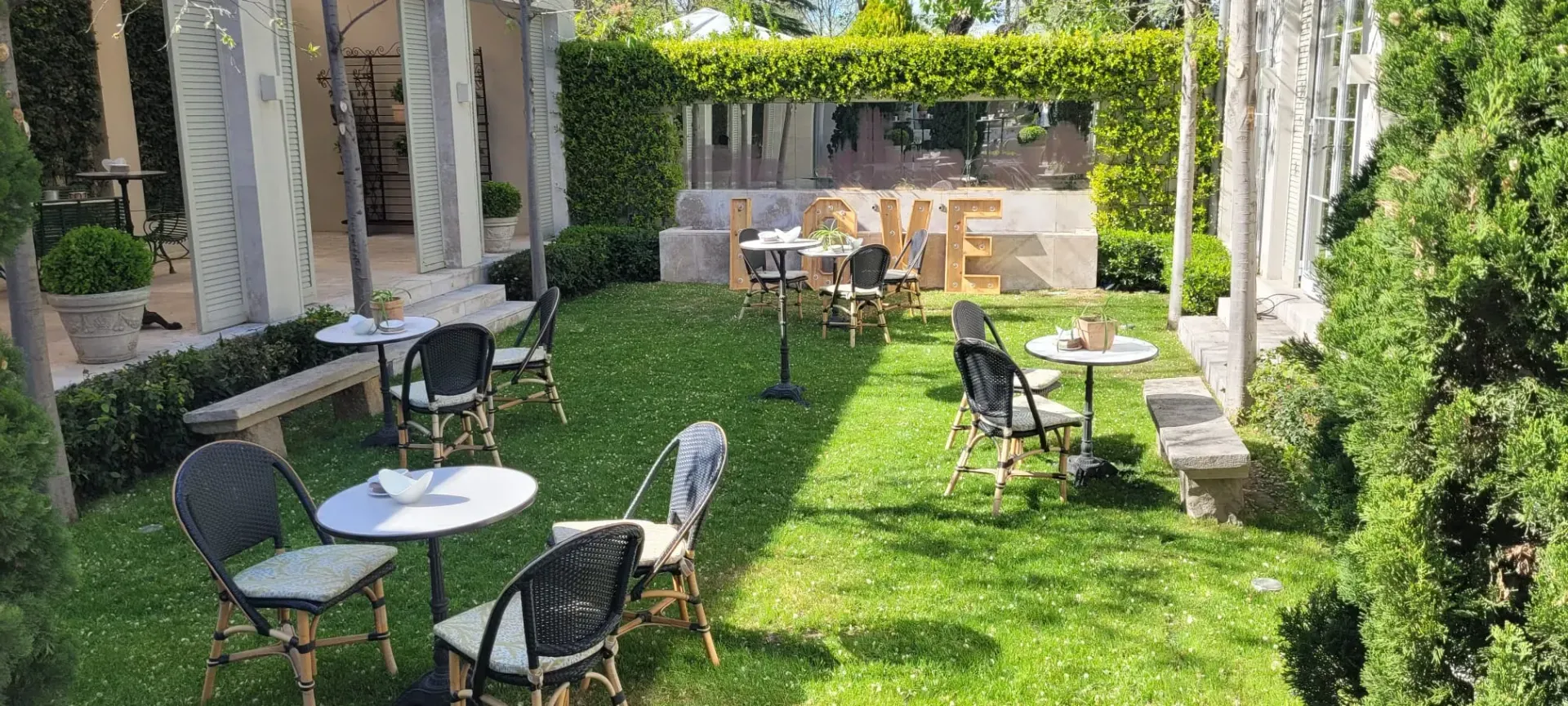 Jardín soleado con patio, mesas, sillas y enredaderas en un entorno de patio.
