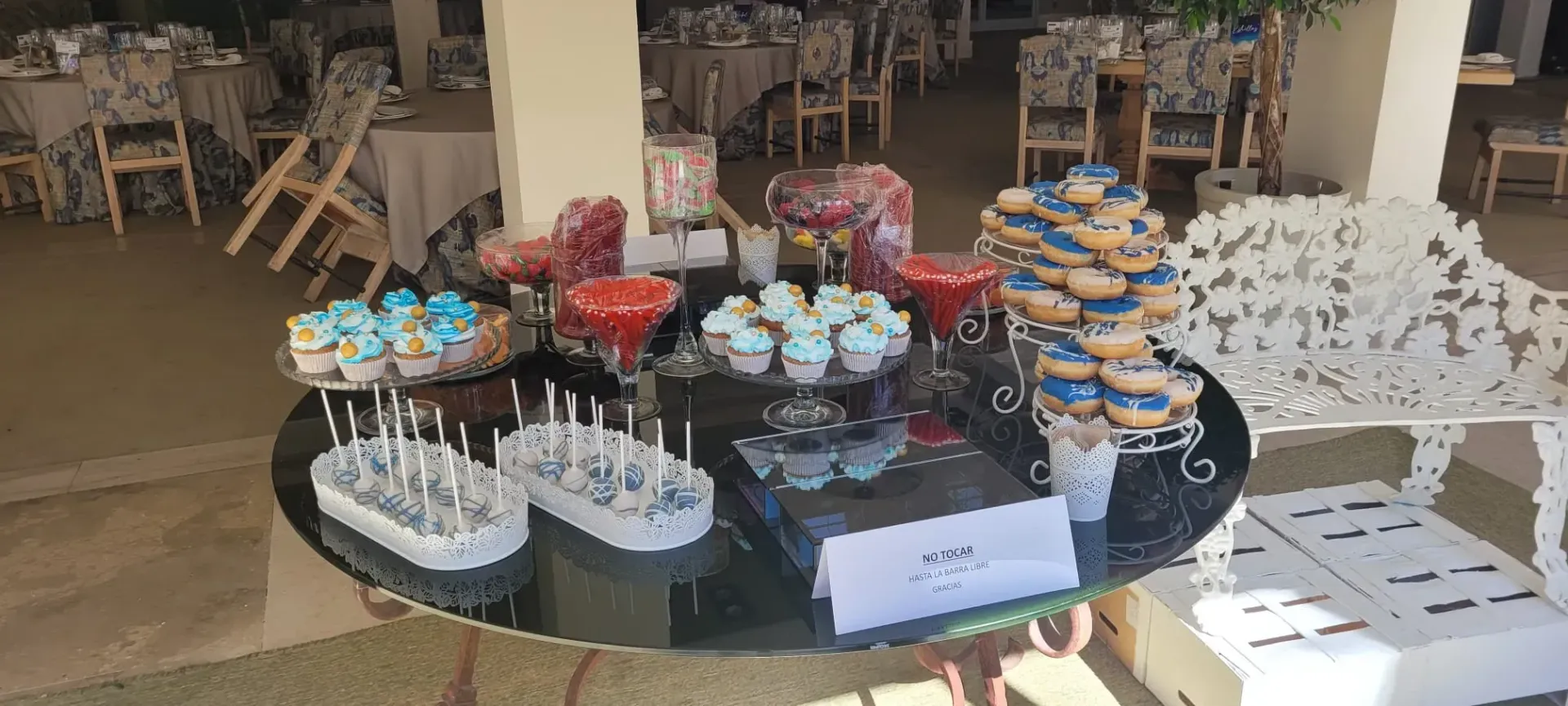Mesa de postres con cupcakes, galletas y dulces dispuestos en una vitrina redonda negra en una cafetería.