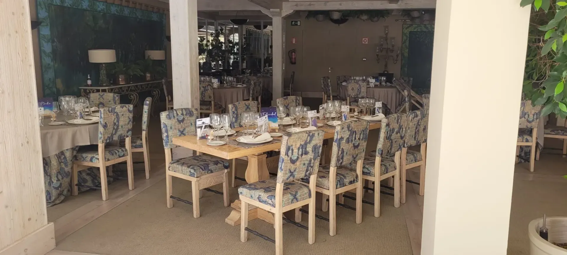Zona de comedor al aire libre con mesas y sillas de madera dispuestas para los comensales bajo un patio sombreado.