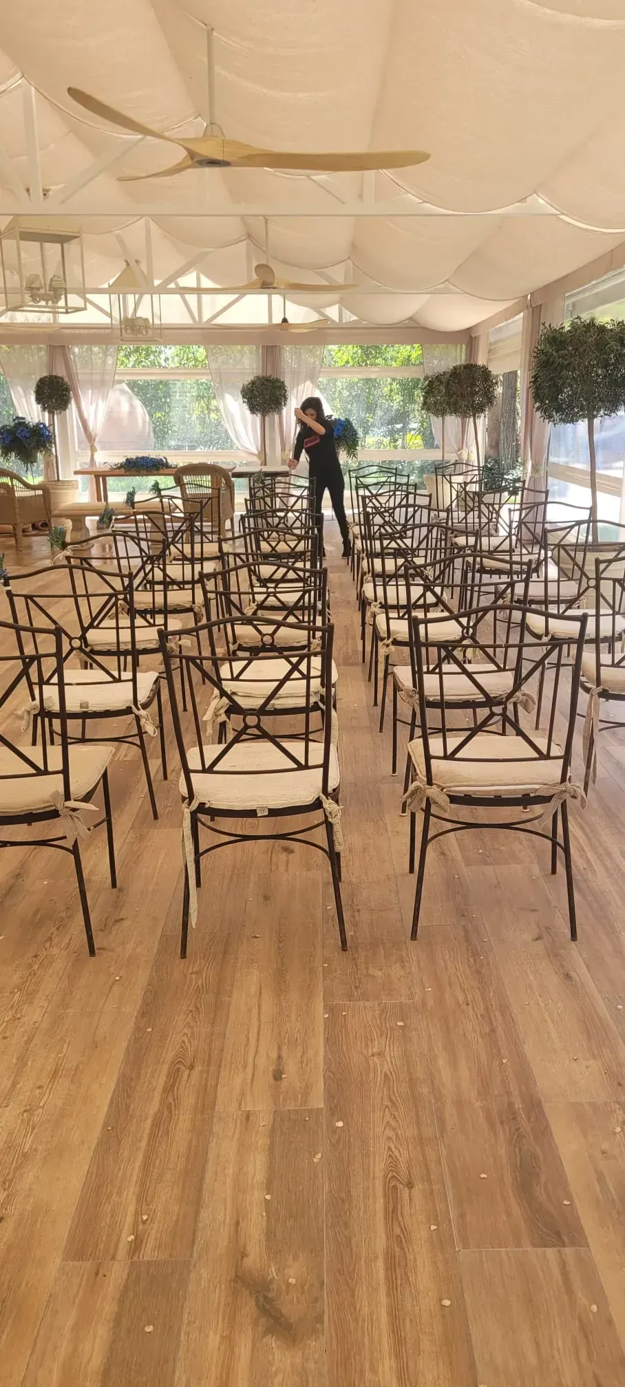 Carpa vacía para eventos con filas de sillas y una pista de baile de madera bajo una tela blanca drapeada y luces de cadena.