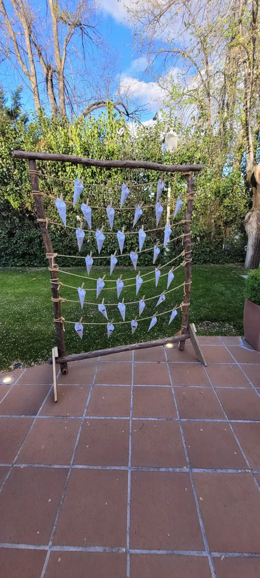 Pinzas de ropa sujetan una cuadrícula de mariposas de papel blanco en un marco de madera en un patio de jardín.