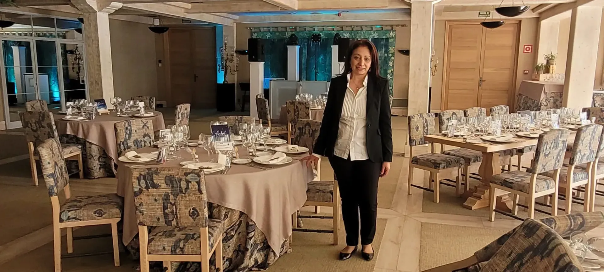 Persona de pie en un elegante restaurante con mesas puestas y sillas ornamentadas.