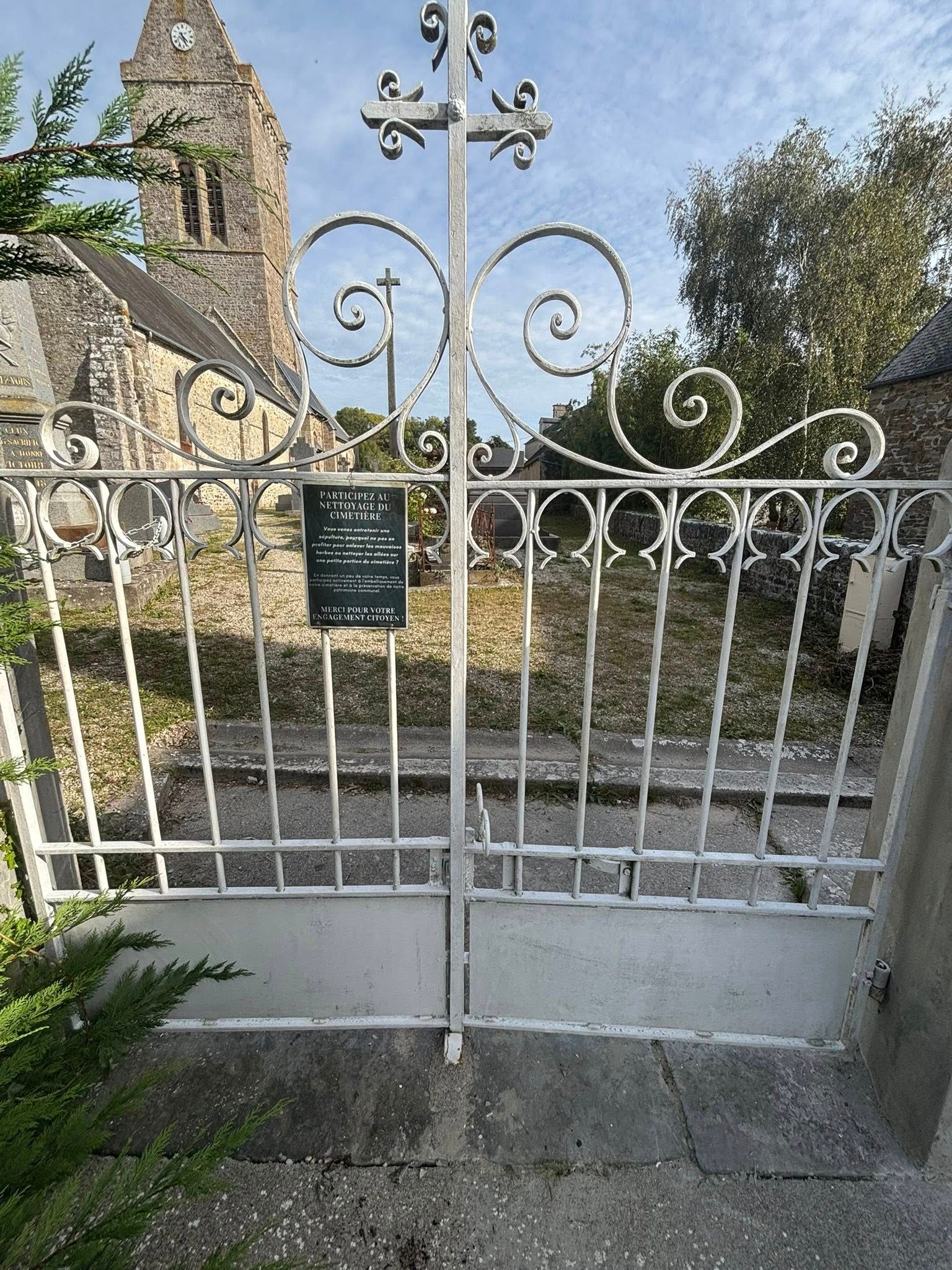 Portail en fer forgé blanc donnant sur un cimetière avec une église en arrière-plan.