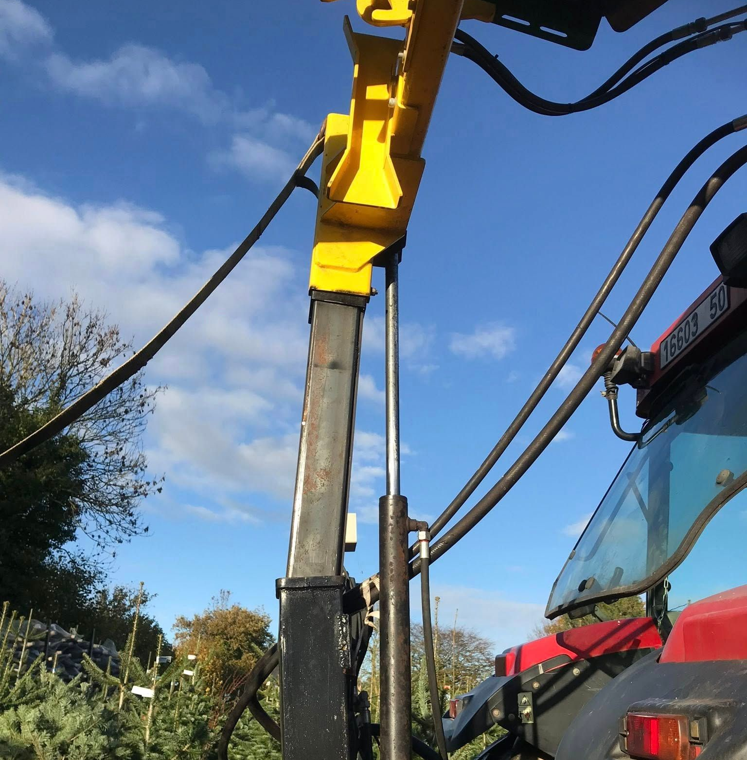 Bras d'une machine agricole jaune et noir à côté de la cabine d'un tracteur rouge.