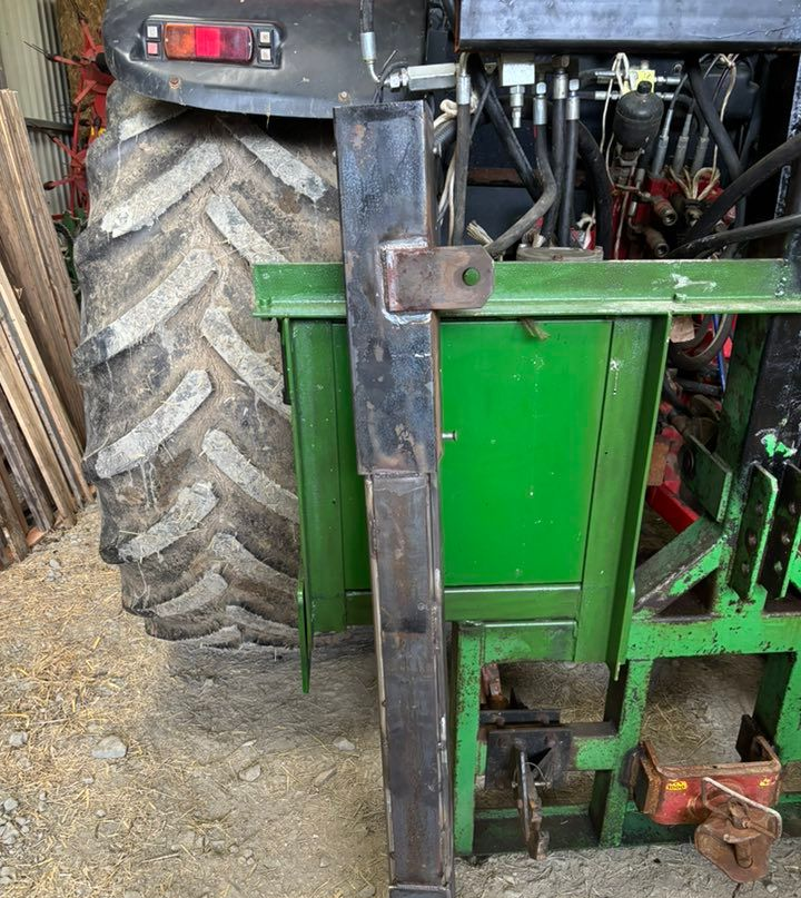 Support métallique noir fixé à un tracteur vert.