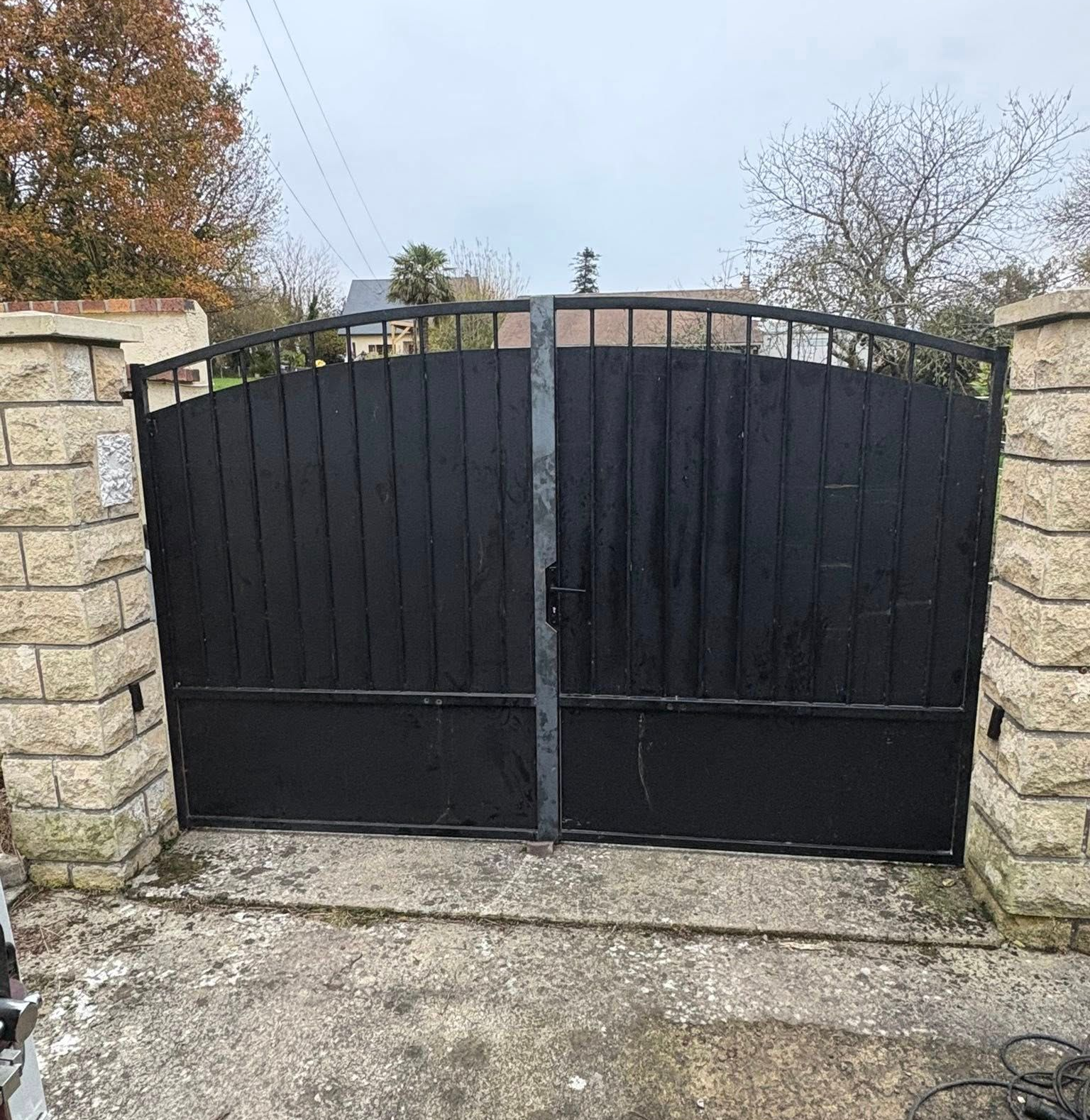 Portail métallique noir, encadré par des piliers en pierre.