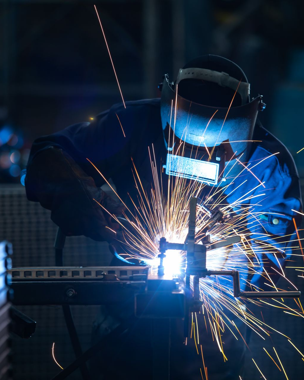 Un soudeur portant un masque travaille avec des étincelles dans un atelier.