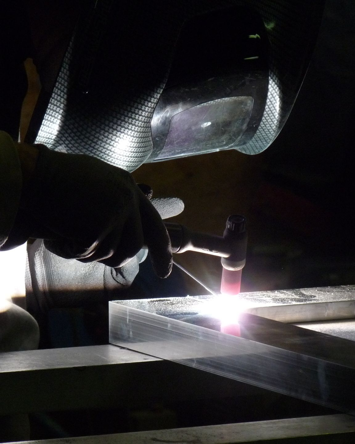 Soudeur portant un masque de protection, travaillant du métal ; une lumière vive éclaire la zone de travail.