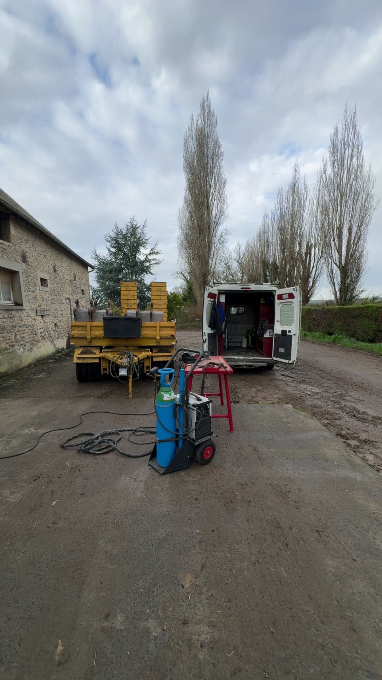 Une personne en combinaison bleue soude du métal, portant un casque et des gants de soudeur.
