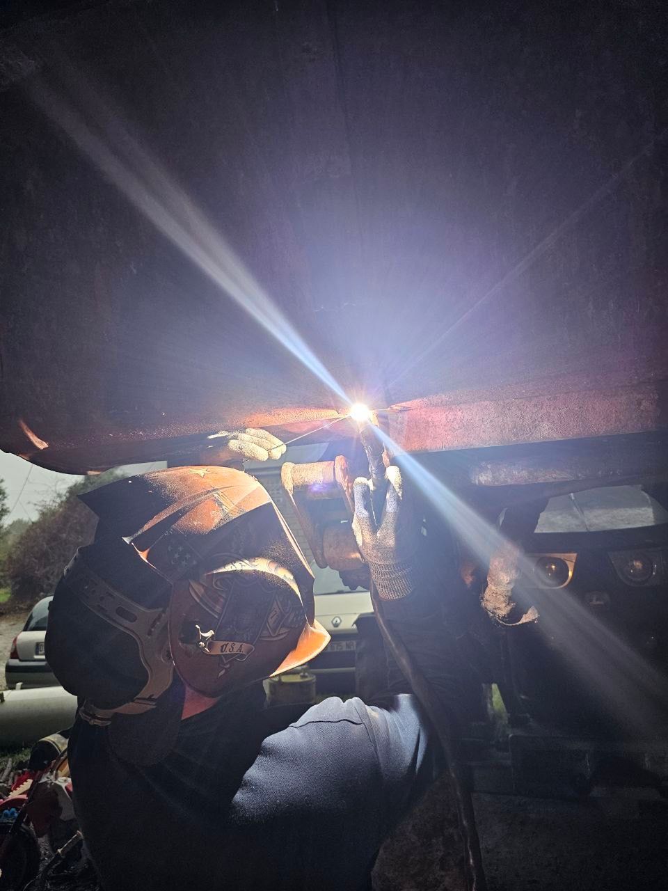 Soudeur en tenue de protection travaillant sur du métal, des étincelles jaillissent.