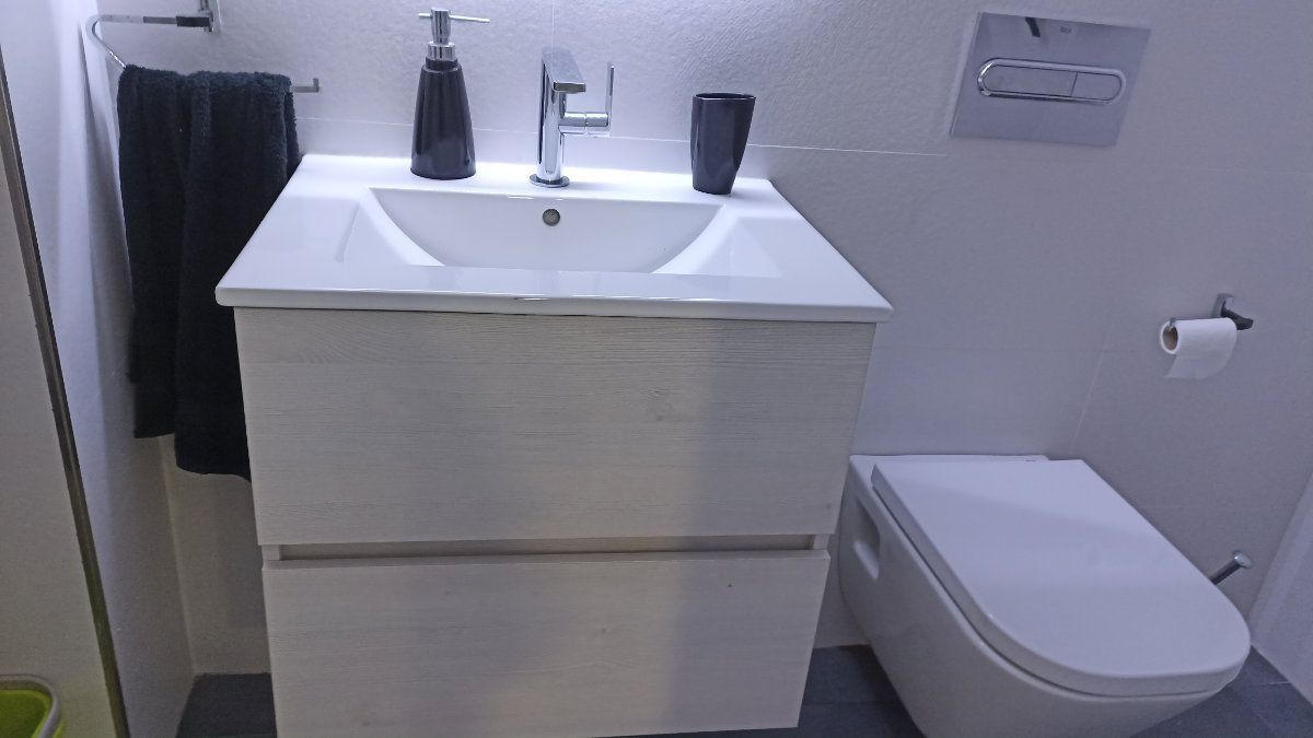 Baño con lavabo y mueble blanco, toallas negras, inodoro.