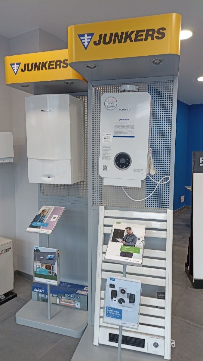 Exhibición de calentadores de agua Junkers y folletos en una tienda, con marca amarilla y un estante blanco y gris.