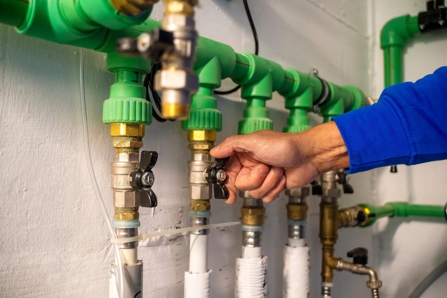 Ajuste manual de una válvula en tuberías verdes en un cuarto de servicio.