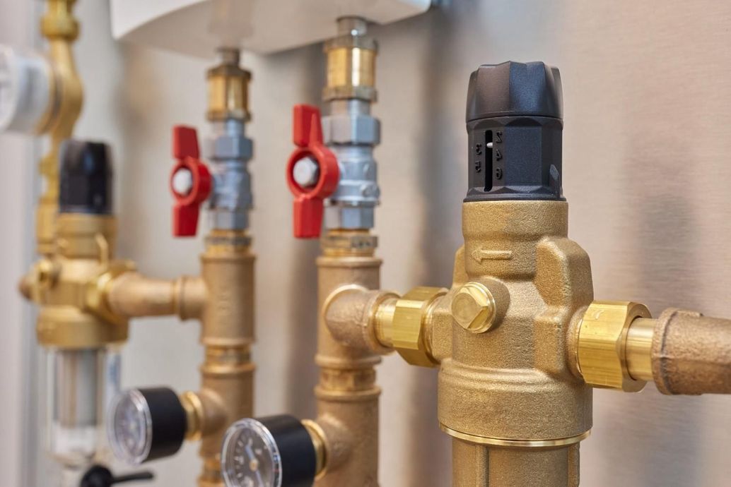 Válvulas y tuberías de latón con manetas rojas en un sistema montado en la pared.