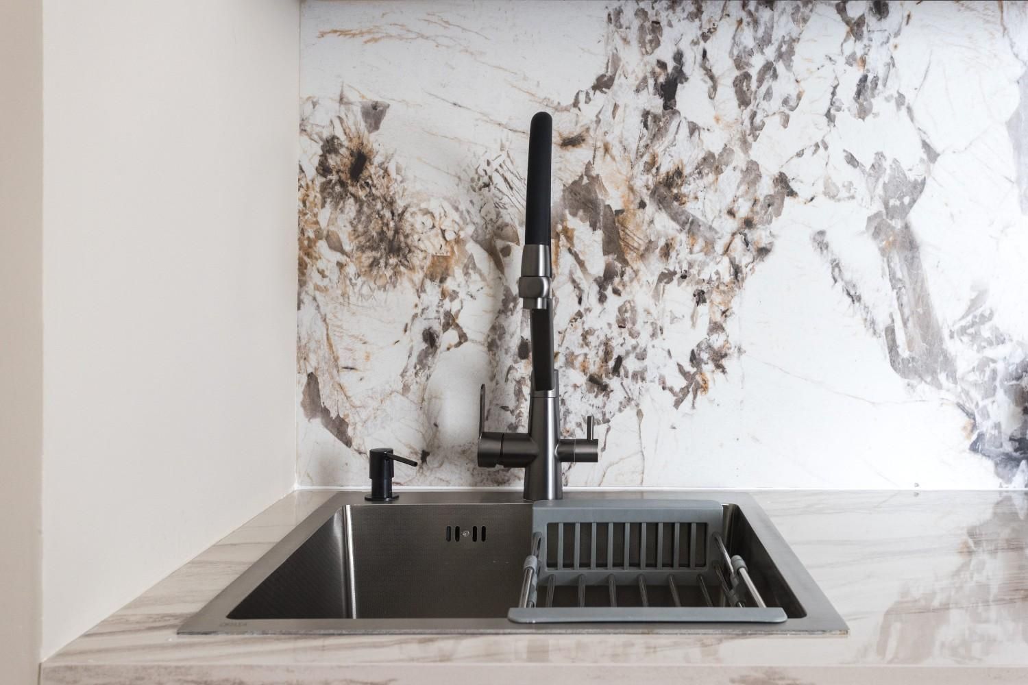 Fregadero de cocina moderno con grifo negro y protector contra salpicaduras de mármol.