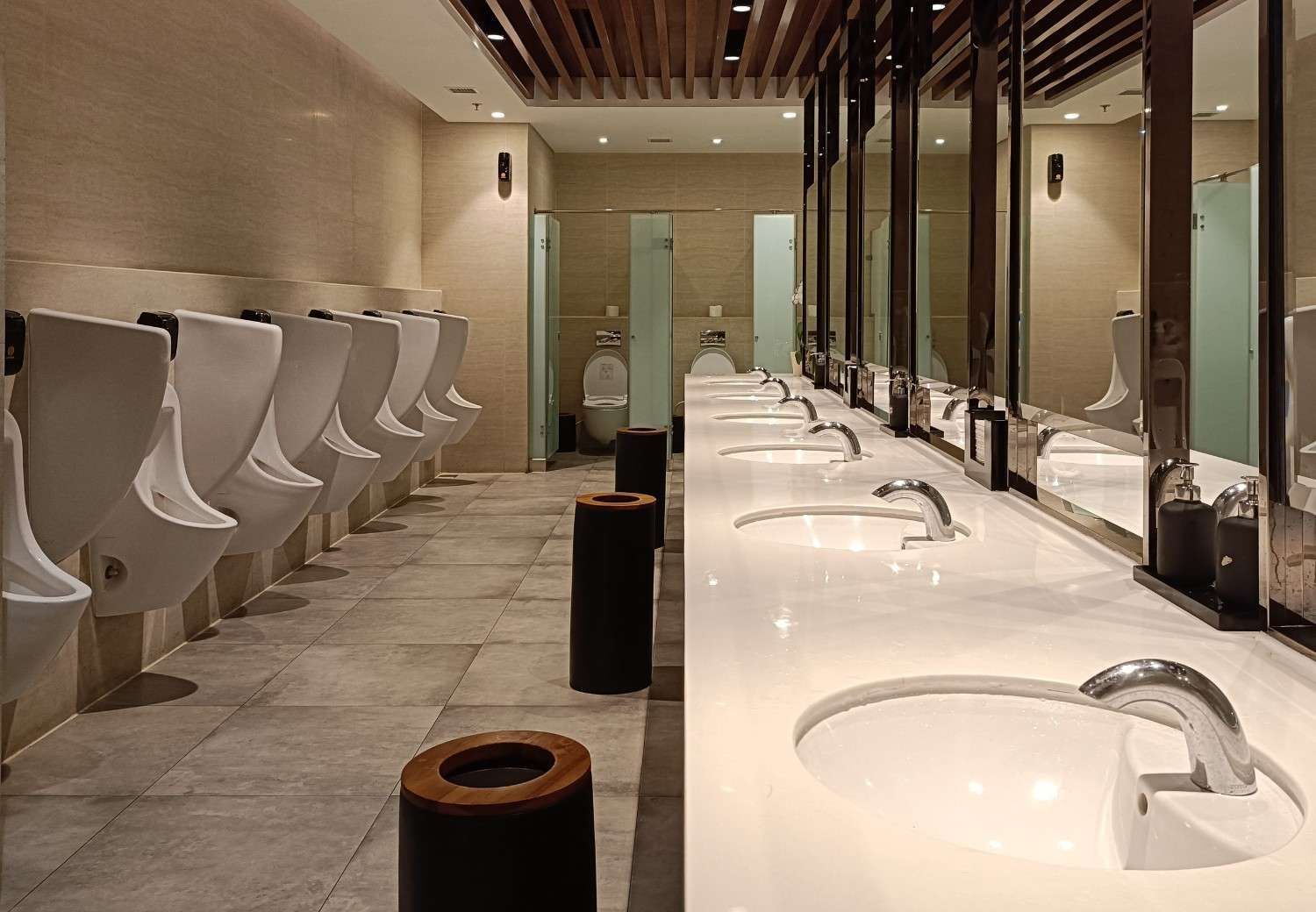 Baño moderno con urinarios a la izquierda, lavabos a la derecha y una pared con espejo.