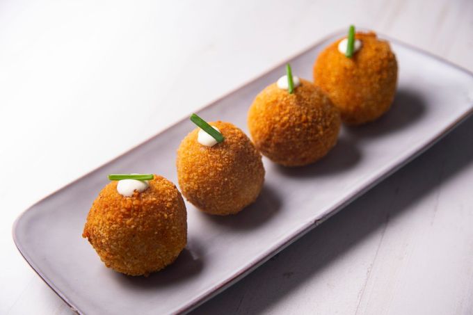 Cuatro aperitivos fritos de color marrón dorado en un plato rectangular, cada uno coronado con una guarnición verde.