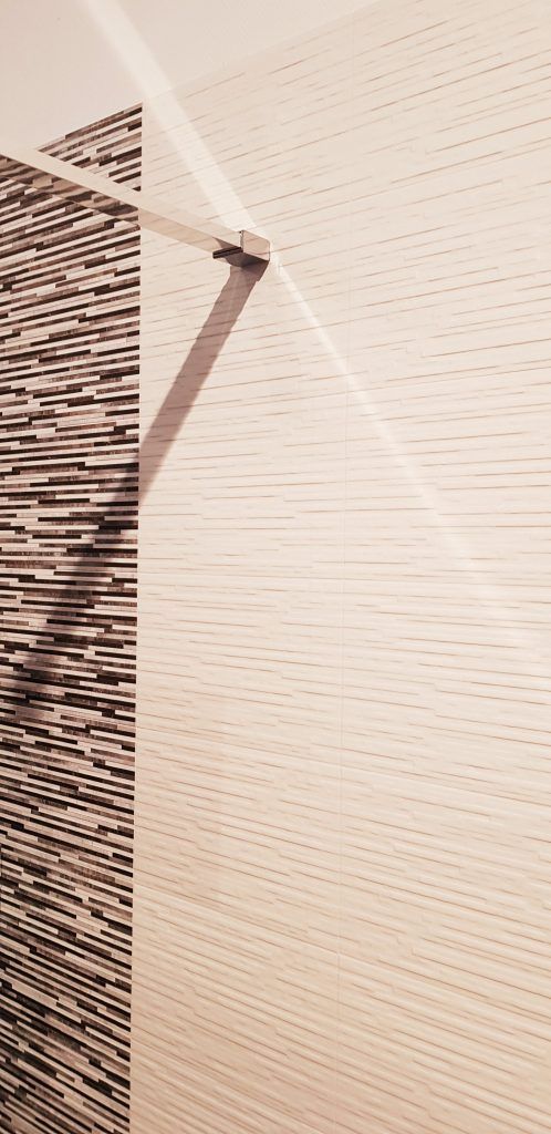 Gros plan sur un mur beige texturé avec un luminaire métallique foncé et incurvé et des lignes d'ombre diagonales.