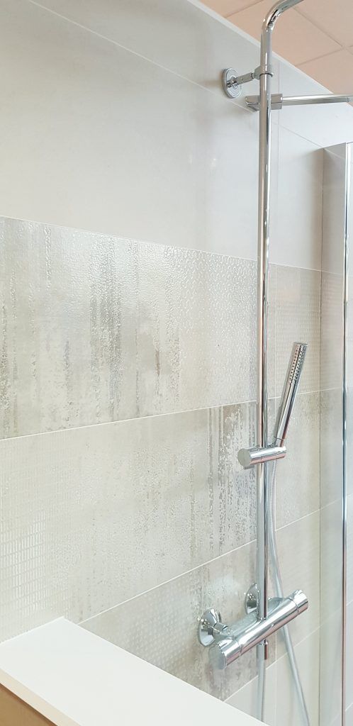Douche moderne avec porte en verre, robinetterie chromée et mur carrelé en pierre claire.