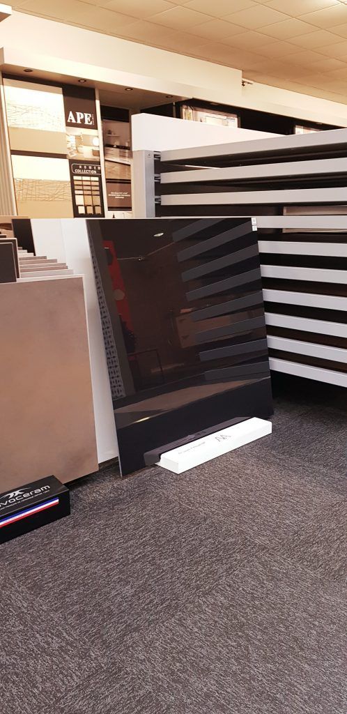 Un téléviseur à écran plat noir est posé contre un meuble dans une allée de magasin, à côté d'étagères à rayures et d'un sol recouvert de moquette.