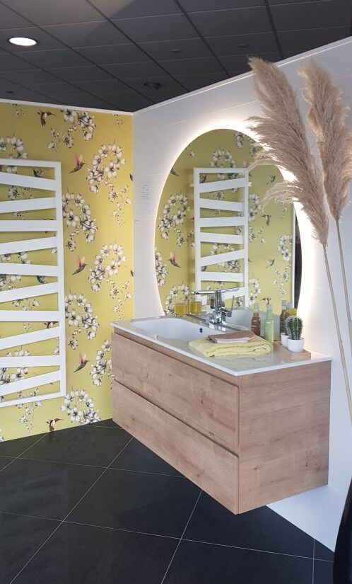 Espace coiffeuse moderne avec meuble en bois, miroirs arqués, échelles blanches, papier peint fleuri jaune et herbes de la pampa.