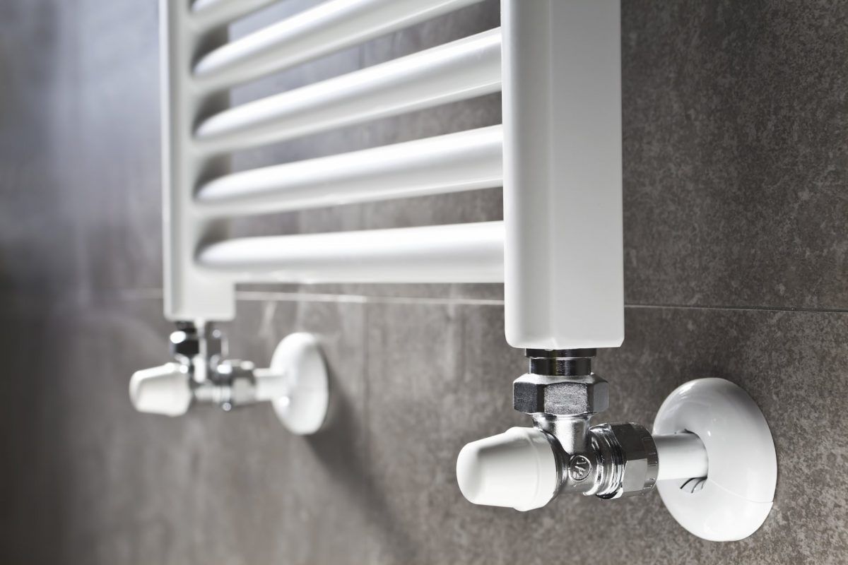 Radiateur de salle de bains blanc avec robinetterie chromée, contre un mur carrelé gris.