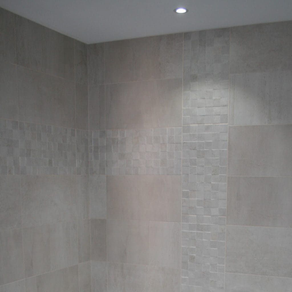 Mur de douche carrelé gris avec un plafonnier encastré au-dessus