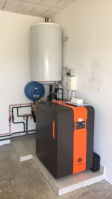 Chaufferie avec réservoir d'eau blanche, groupe de chauffage noir et orange, et tuyauterie apparente sur une petite plateforme