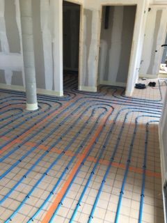 Chantier de construction avec des tuyaux de chauffage au sol installés dans une pièce en rénovation.