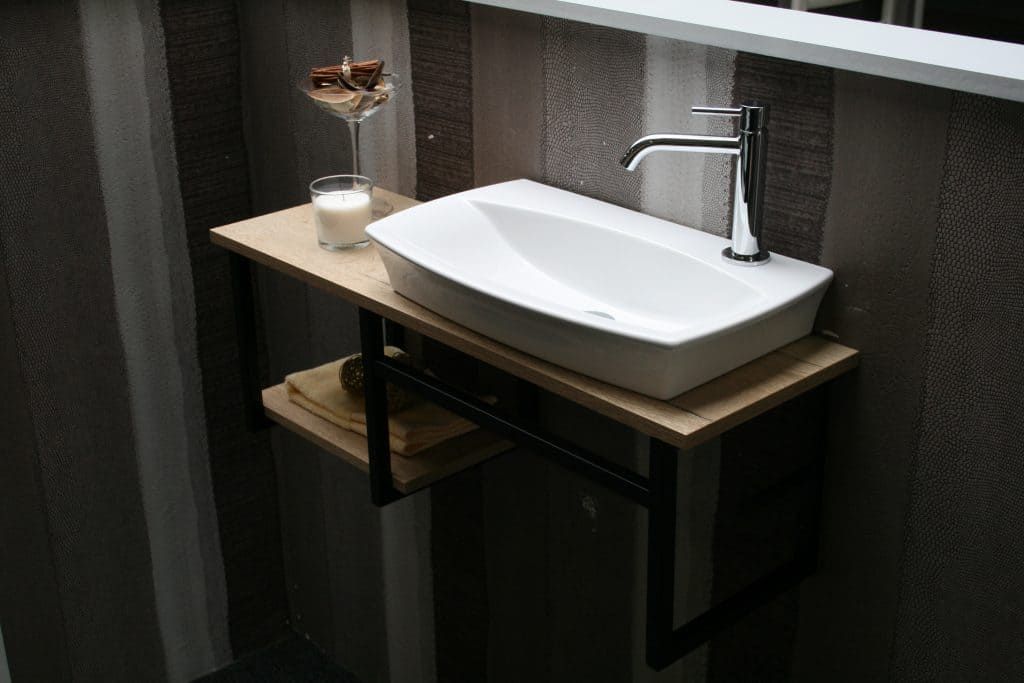 Lavabo de salle de bain moderne avec vasque blanche, robinet chromé, mur foncé et verre d'eau sur le comptoir.