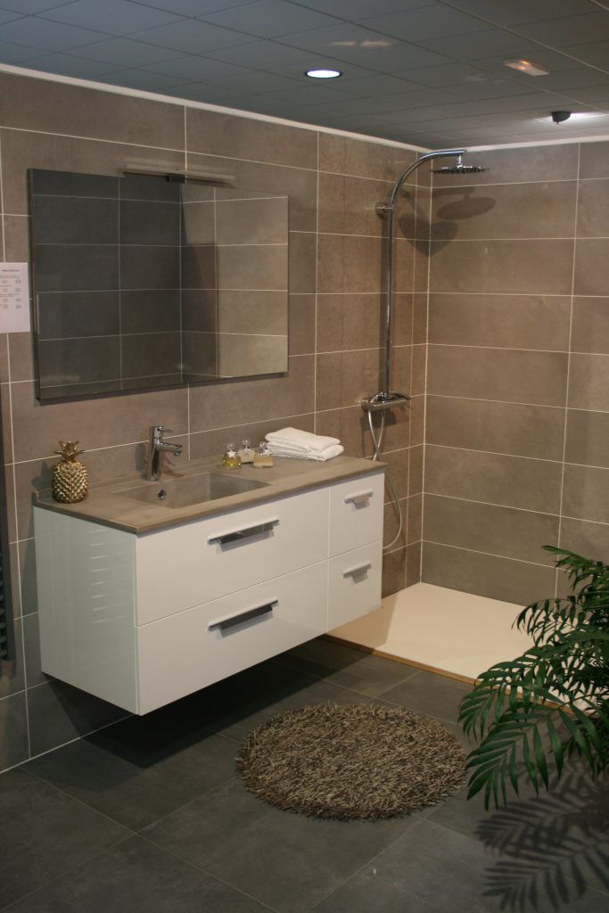 Meuble-lavabo moderne avec miroir, tiroirs blancs, murs carrelés beiges et petit tapis rond.