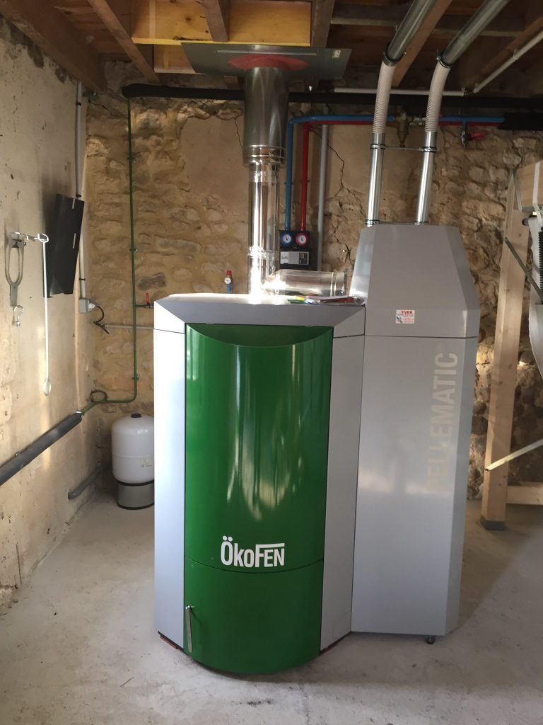 Chaudière de chauffage Green OkoFEN avec unité grise dans une buanderie au sous-sol, raccordée à des conduits d'évacuation métalliques