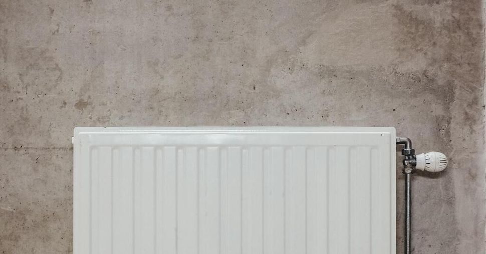 Radiateur blanc contre un mur beige rugueux, avec un robinet d'arrêt visible sur la droite.