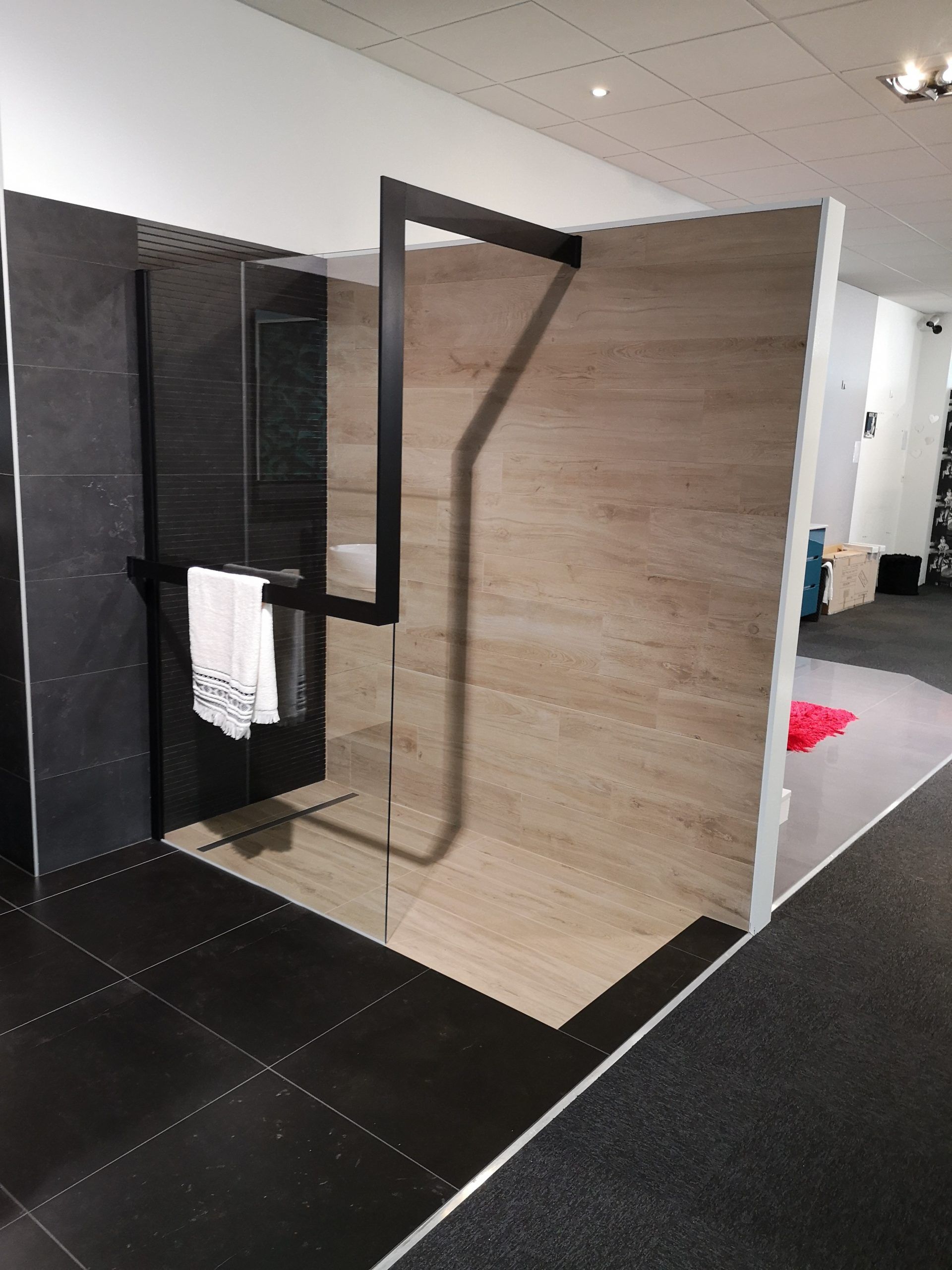 Cabine de douche moderne avec porte en verre noir, panneau mural imitation bois et sol carrelé.