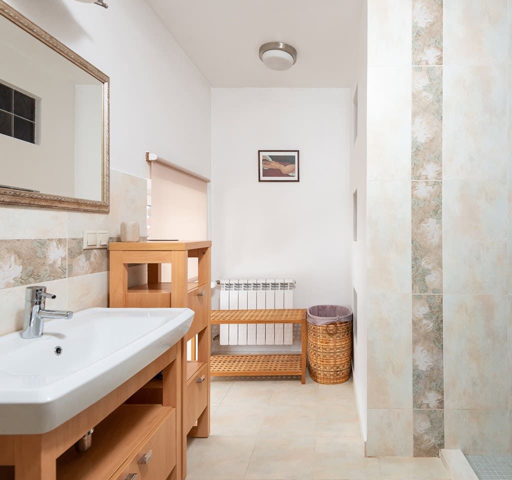 Salle de bain lumineuse avec lavabo, miroir, étagères en bois, banc et panier en osier dans des tons neutres.