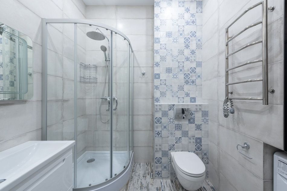 Salle de bain moderne blanche avec douche en verre, toilettes, lavabo, porte-serviettes et mur d'accent en carrelage bleu à motifs