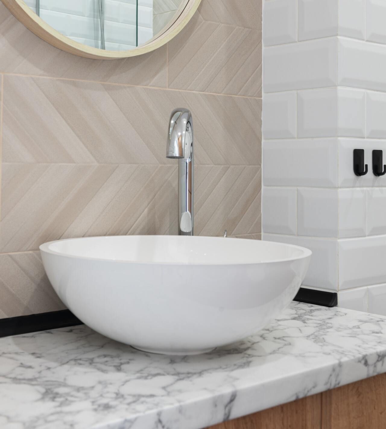 Vasque blanche avec robinet chromé sur un comptoir de salle de bain en marbre et un mur carrelé, à côté d'un miroir.