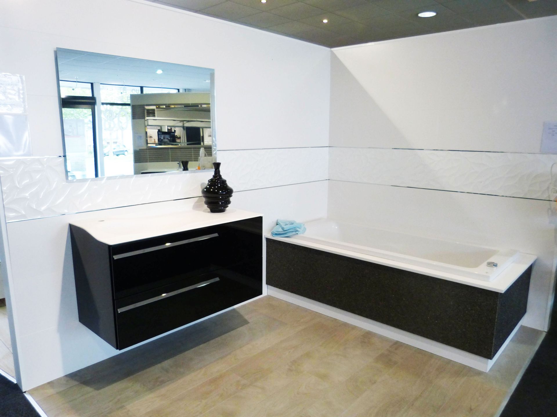 Salle de bains moderne avec meuble-lavabo noir, baignoire blanche, miroir mural et carrelage beige au sol
