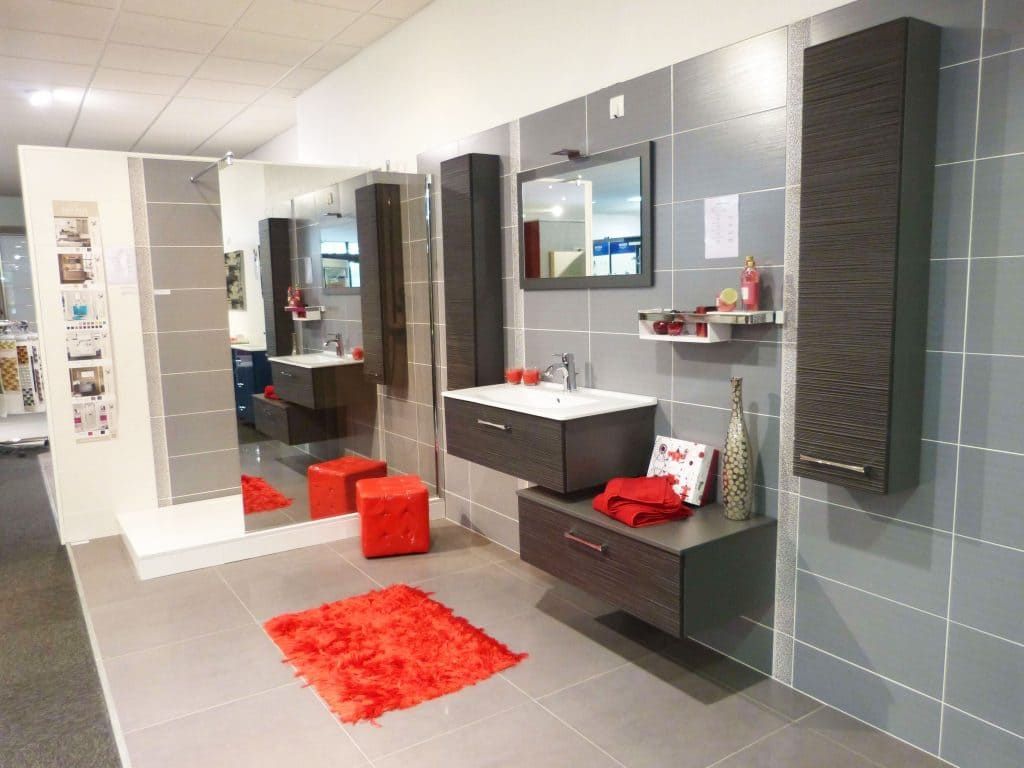 Salle de bains moderne grise avec meuble-lavabo noir, miroirs, tabourets rouges et tapis rouge dans un intérieur carrelé