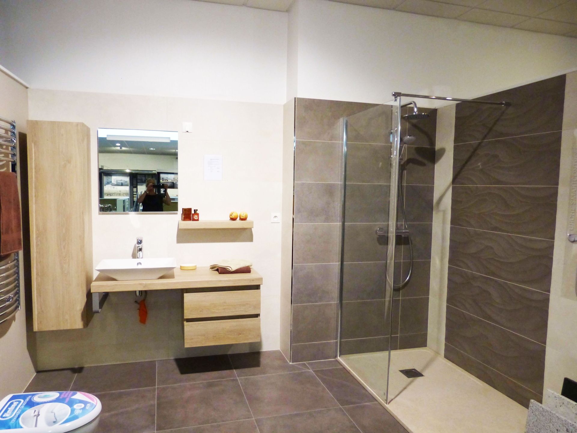 Salle de bains moderne avec carrelage marron, douche en verre, meuble-lavabo suspendu et miroir sur un mur blanc