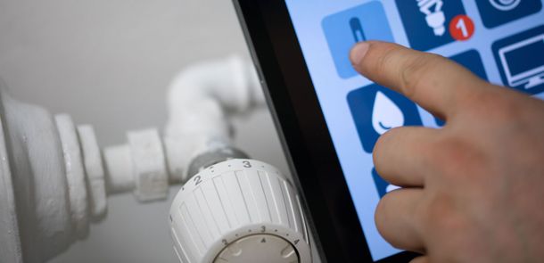 Main appuyant sur le thermostat d'une maison connectée via une tablette