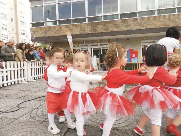Un grupo de niños con tutús rojos y blancos bailan frente a un edificio.