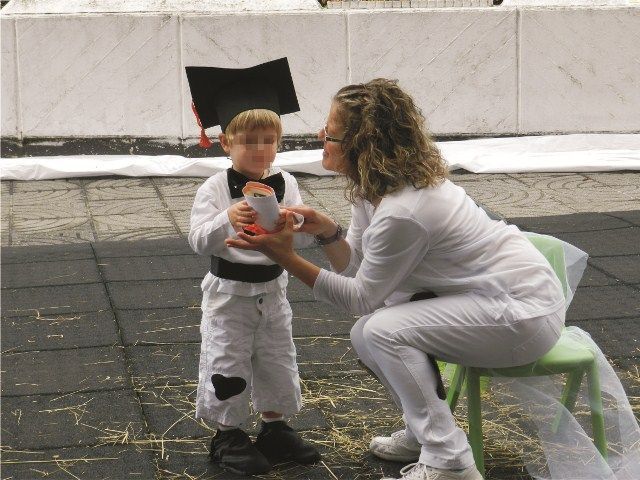 Una mujer está arrodillada junto a un niño que lleva una toga y un birrete de graduación.
