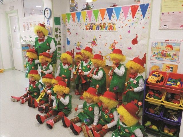 Un grupo de niños vestidos de elfos están sentados en el suelo tocando instrumentos.