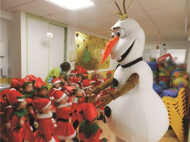Un grupo de niños vestidos con gorros de Papá Noel están de pie alrededor de una mascota de muñeco de nieve.
